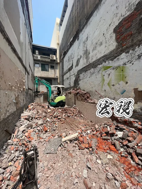 相鄰建物間的拆除現場，可見機具與地面磚石。