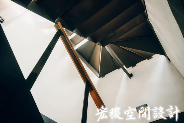 由下仰拍的黑色樓梯與木扶手細節。